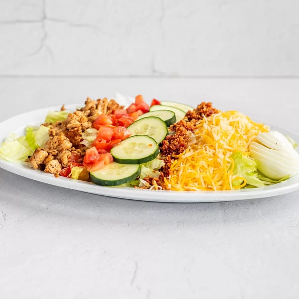 A large American salad with chicken, tomatoes, cucumbers, bacon bits, shredded cheese, and sliced egg.