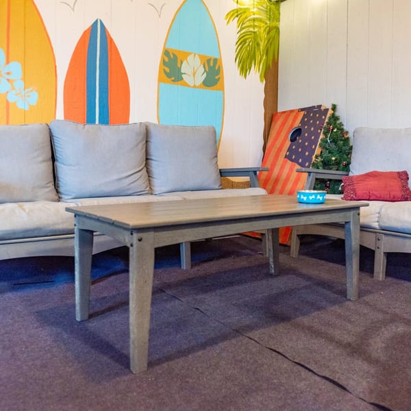 Outdoor seating area with gray sofas, a wooden table, and a surf-themed wall mural.