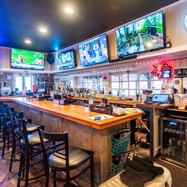 A long wooden bar with black stools, multiple TVs, and bottles of liquor at House Of Sauce.