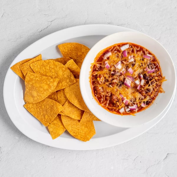 A bowl of chili with shredded cheese and diced red onions, served with tortilla chips.