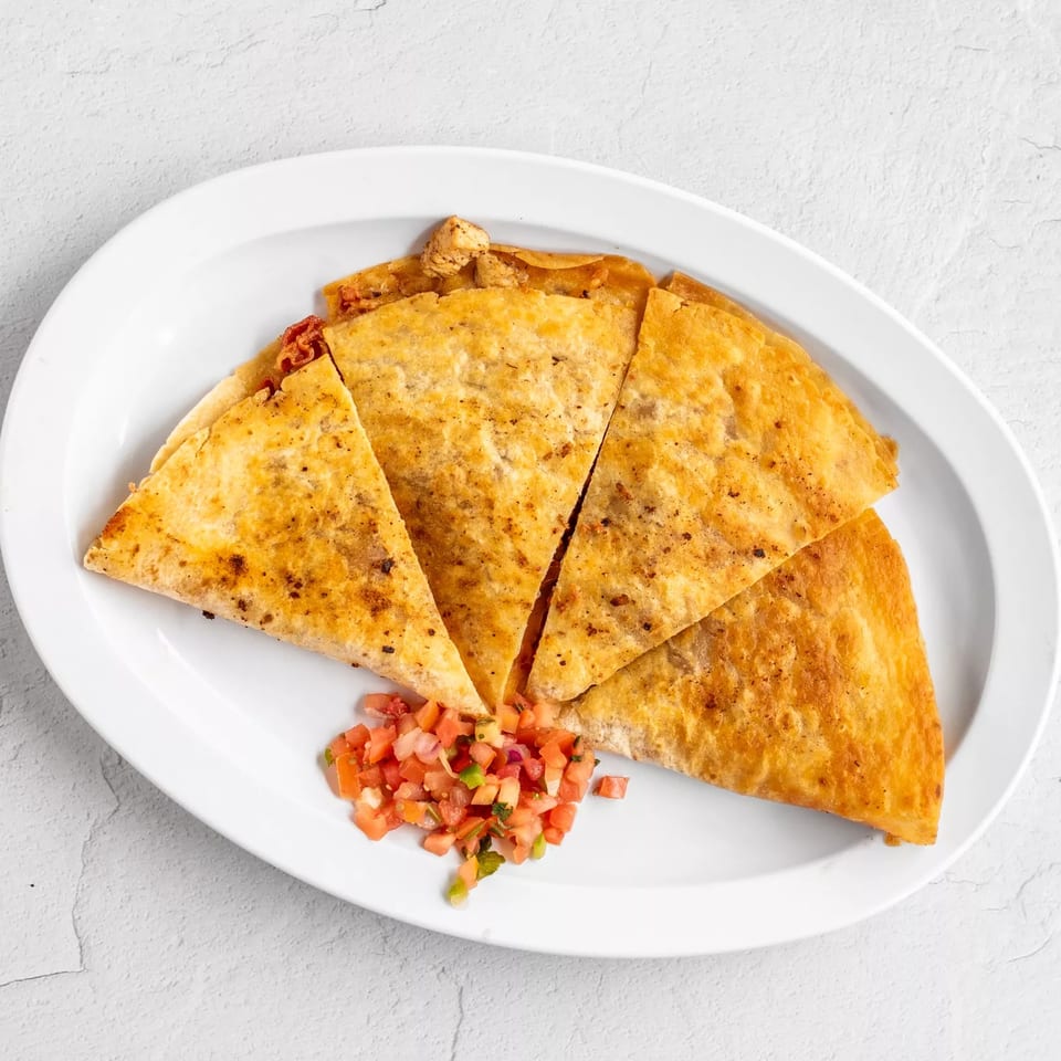 Golden-brown quesadilla wedges with chicken and pico de gallo on a white oval plate.