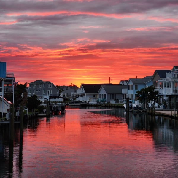 Vibrant red and orange sunset over a canal lined with houses and boats, reflecting in the water.