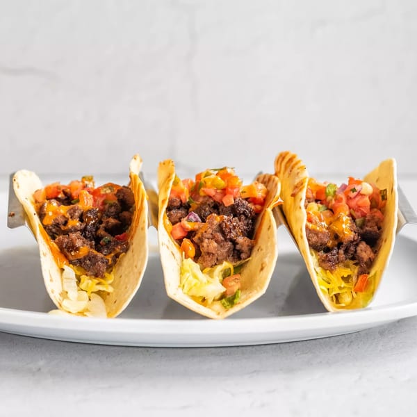 Three House Of Sauce soft tacos filled with ground beef, lettuce, salsa, and a drizzle of sauce.