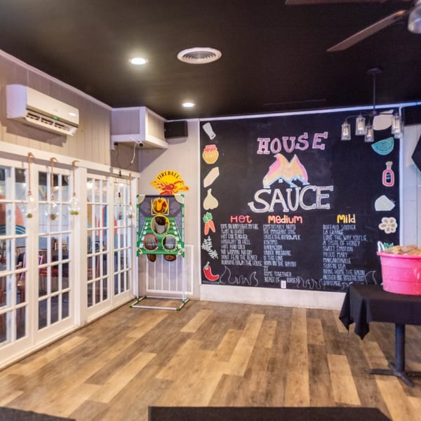 Interior of House Of Sauce with a large chalkboard menu, white French doors, and wooden floors.